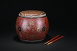 A SMALL RED LACQUER DRUM WITH DRUMSTICKS